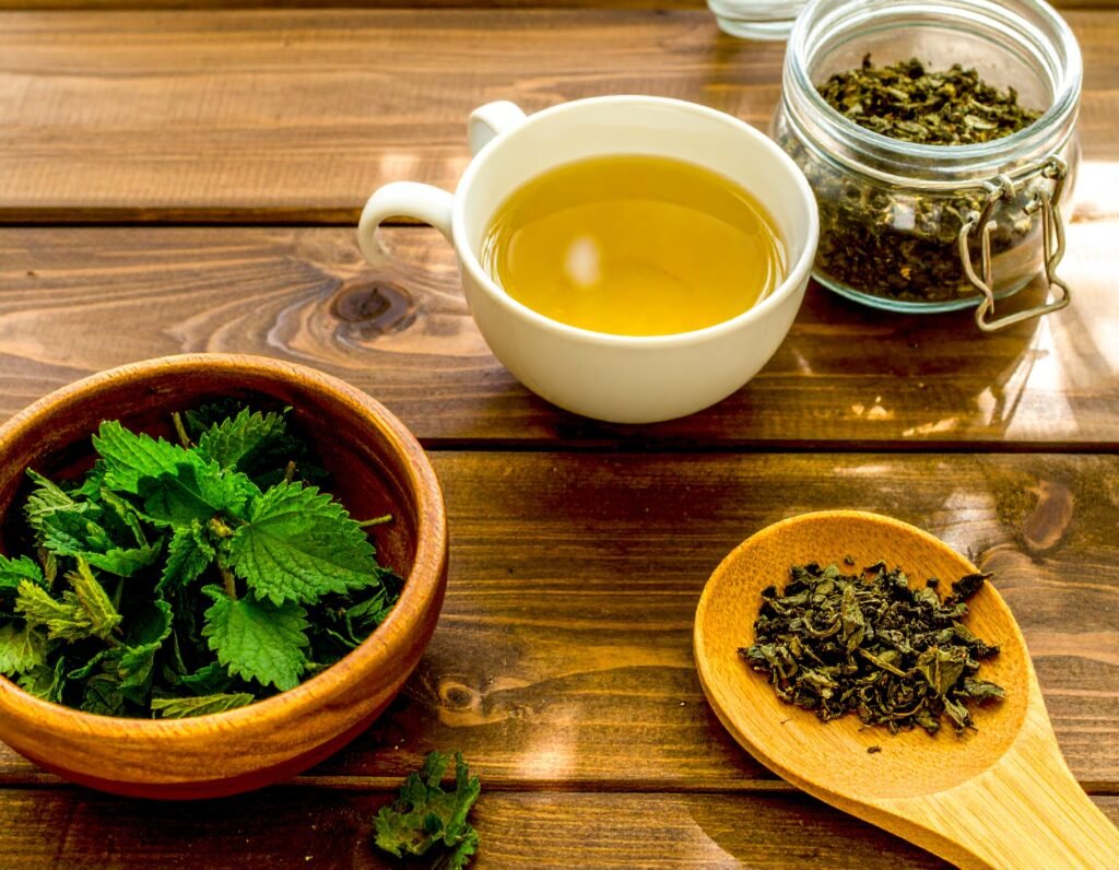 Fresh nettle leaves, steaming mug of nettle tea, and a jar of dried nettle on a wooden table